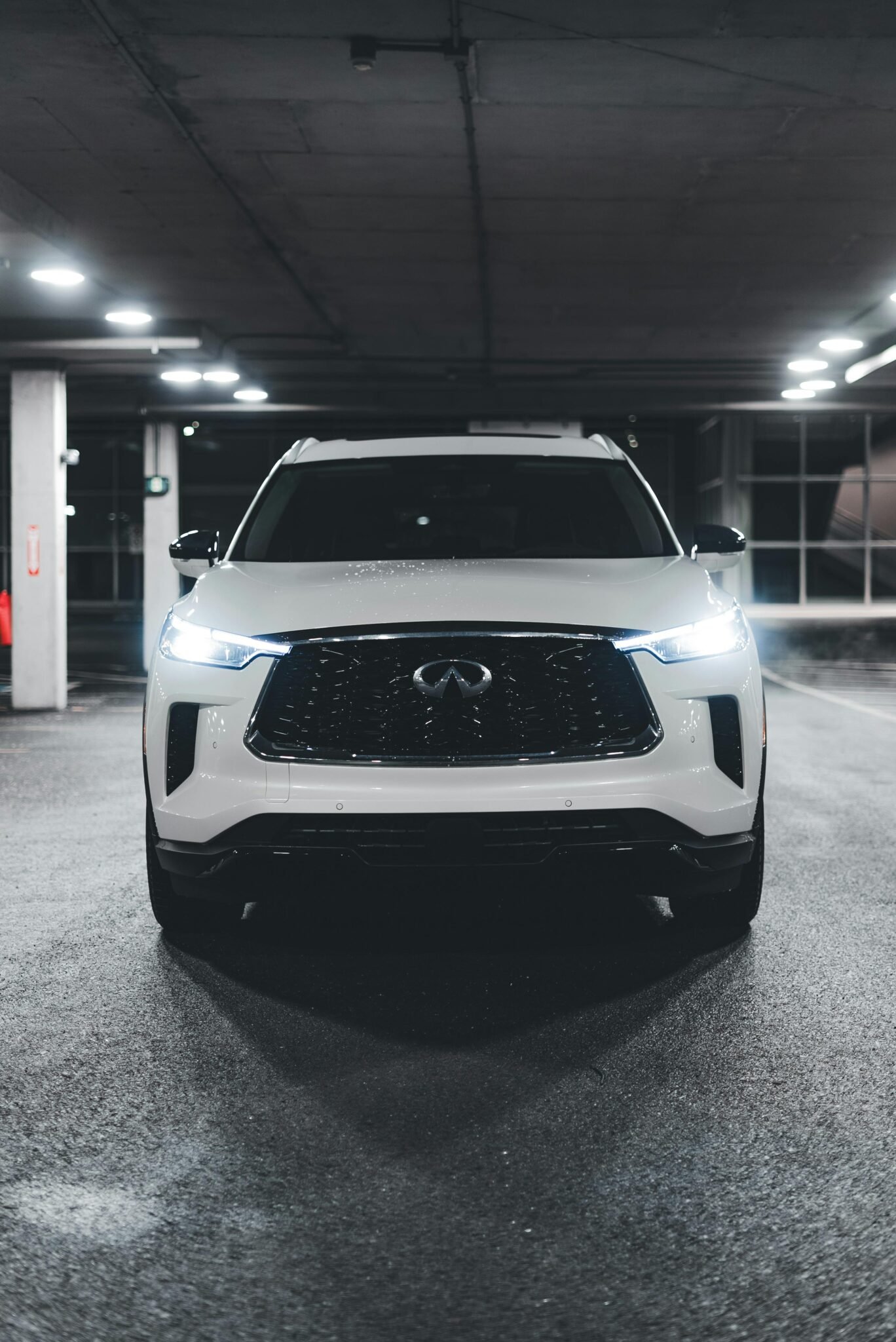 Front view of a stylish white SUV with lit headlights in a dimly lit underground parking garage.